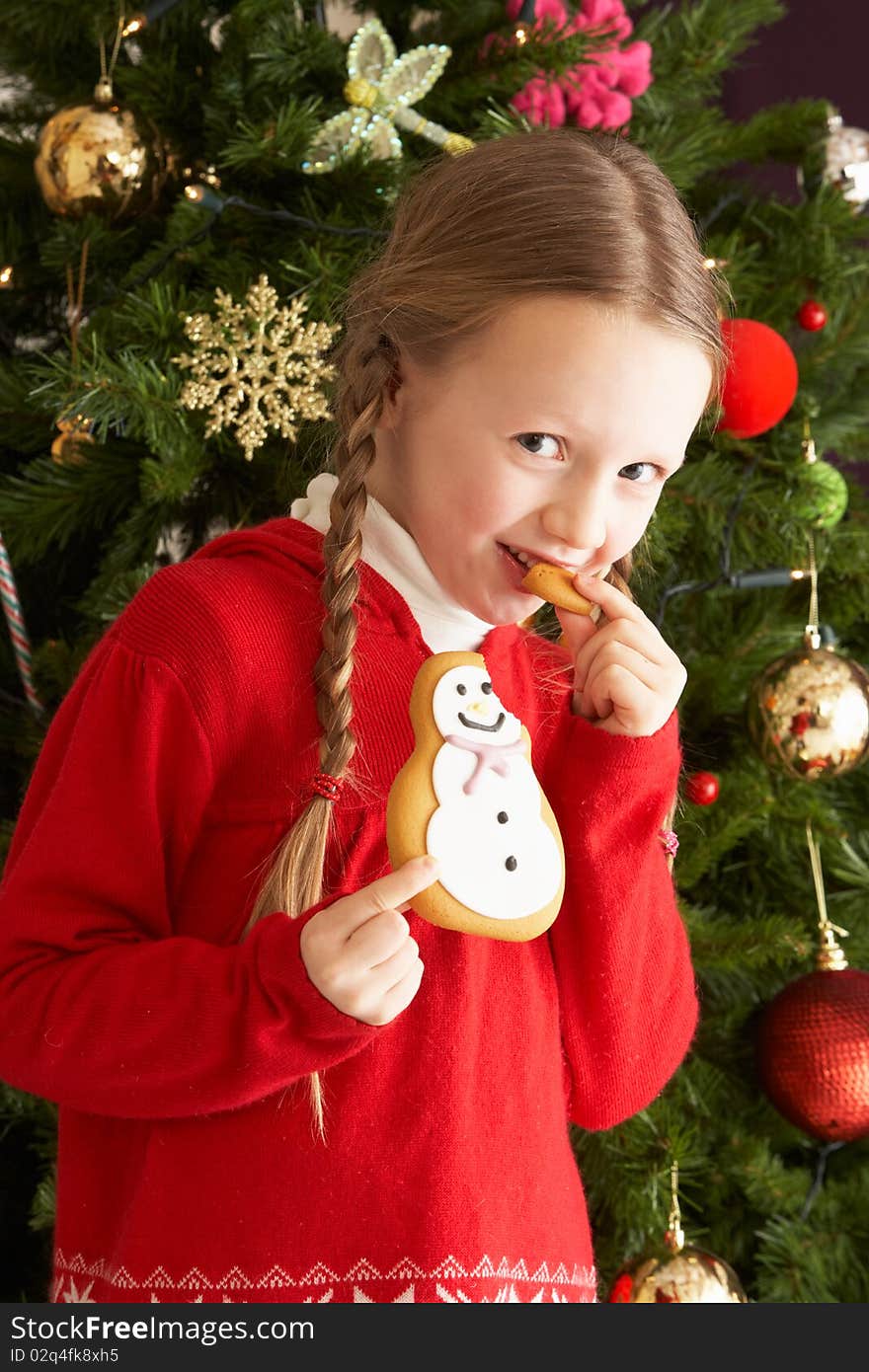 Young Girl Eating Cookie In Front Of Christmas Tree