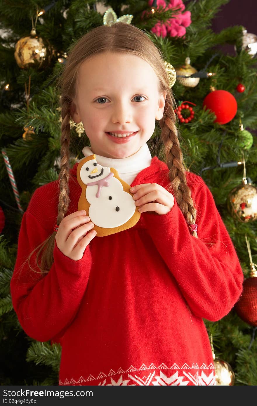 Girl Eating Cookie In Front Of Christmas Tree