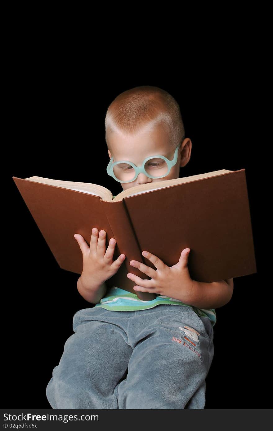 Cute boy with glasses reading a big book isolated on a black background. Cute boy with glasses reading a big book isolated on a black background