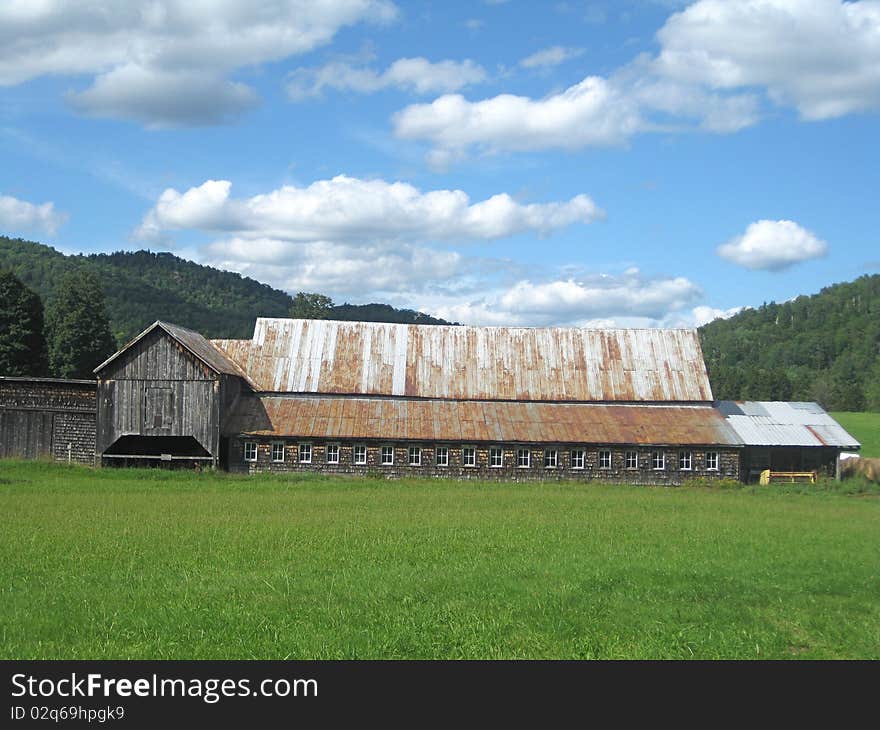 A long barn sits in a field in a valley in Vermont with the mountains in the background. A long barn sits in a field in a valley in Vermont with the mountains in the background.