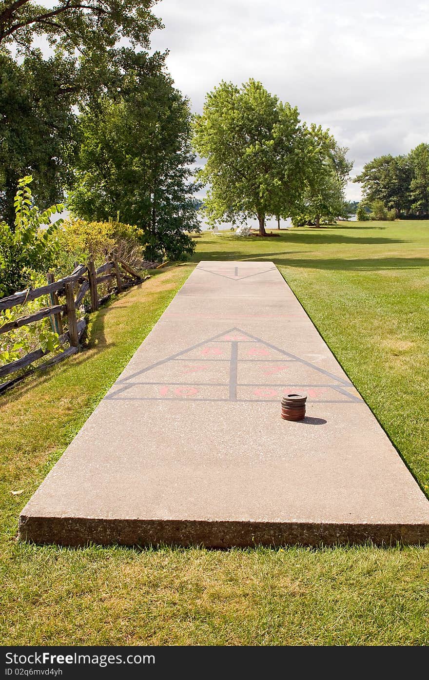 A concrete shuffleboard court in a grassy area at a lakeside resort.