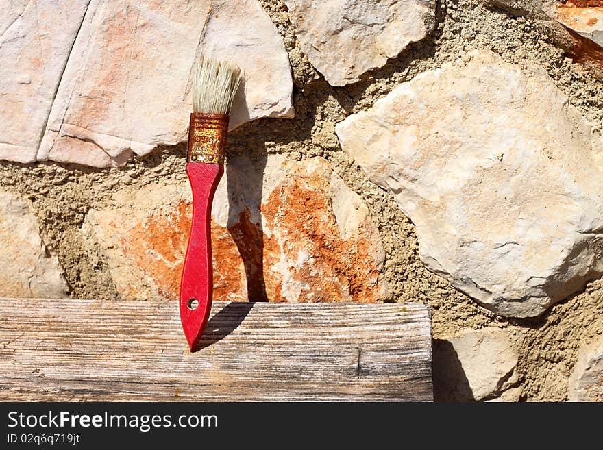 Old red paint brush drying on piece of wood, leaning on stone wall in the sunlight. Old red paint brush drying on piece of wood, leaning on stone wall in the sunlight