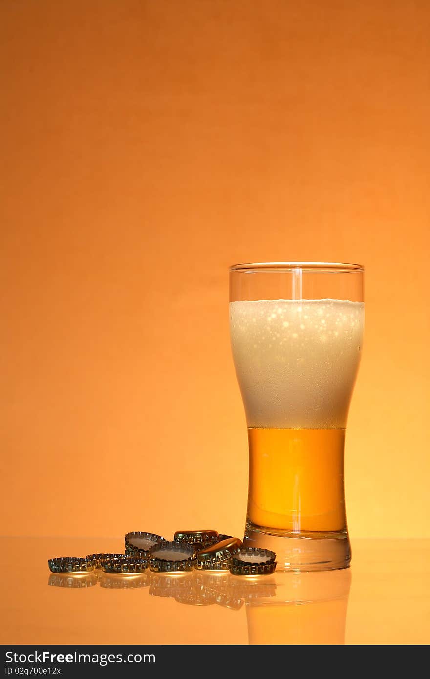 Bottle caps lying near glass of light beer with foam