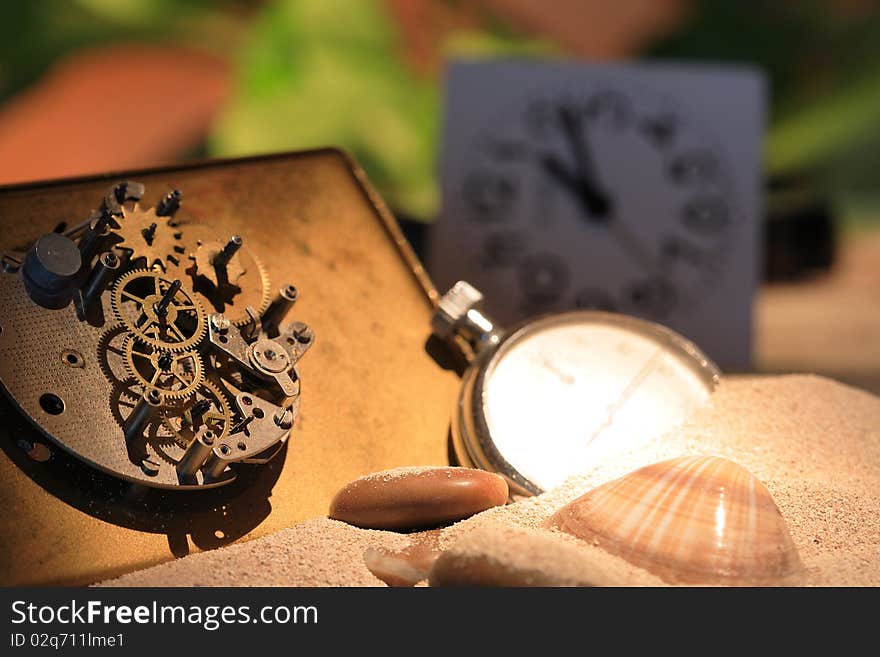 Abstract background with old clock mechanism standing on sand with stones and shells. Abstract background with old clock mechanism standing on sand with stones and shells