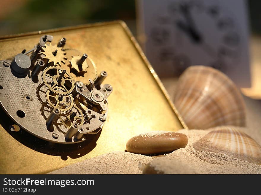 Abstract background with old clock mechanism standing on sand with stones and shells. Abstract background with old clock mechanism standing on sand with stones and shells