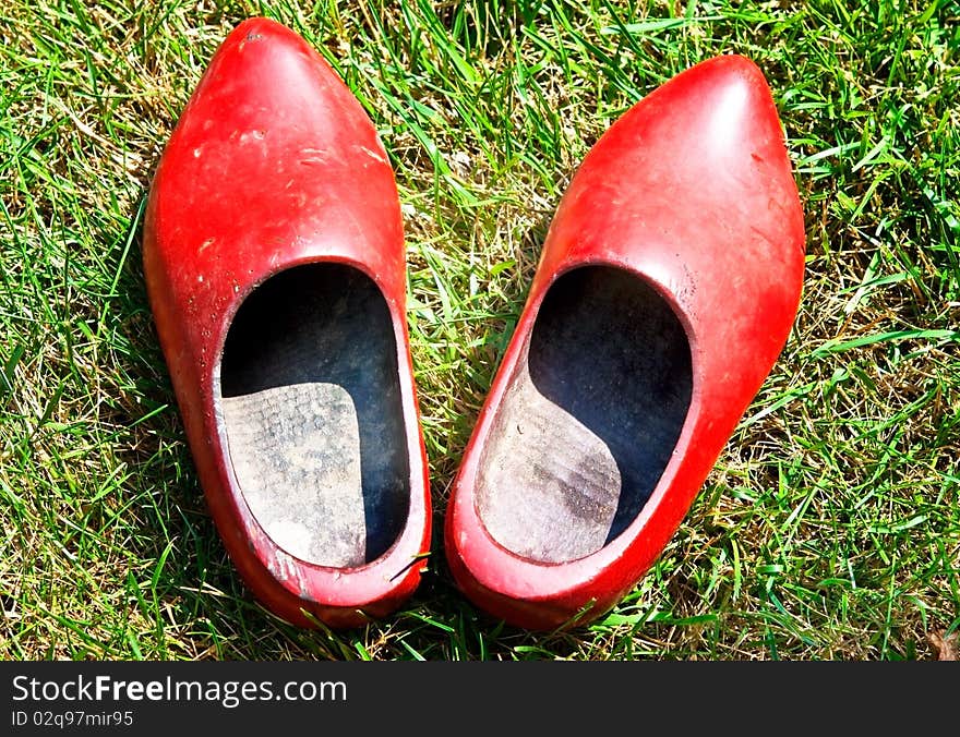 A pair of old, red, wooden shoes in the grass. A pair of old, red, wooden shoes in the grass.