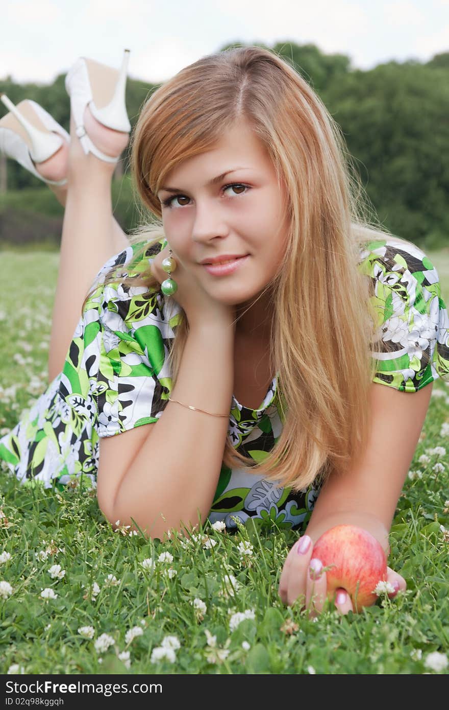 Young beautiful girl relaxing on the field with an apple in his hand. Young beautiful girl relaxing on the field with an apple in his hand