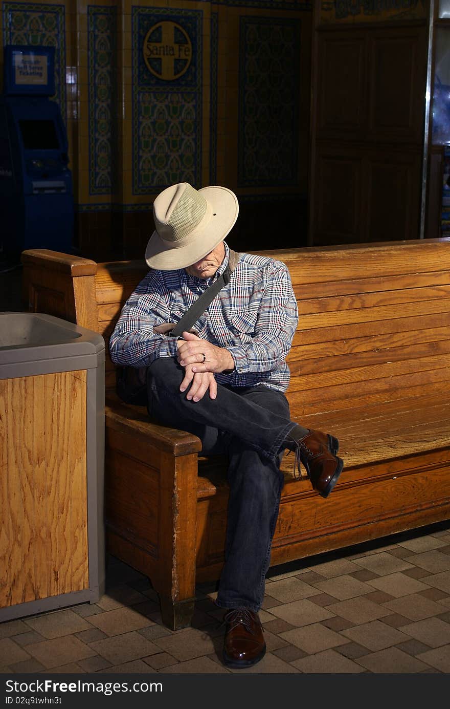 Senior man sitting on a wooden bench in the sun light at a train station waiting for his train. Senior man sitting on a wooden bench in the sun light at a train station waiting for his train