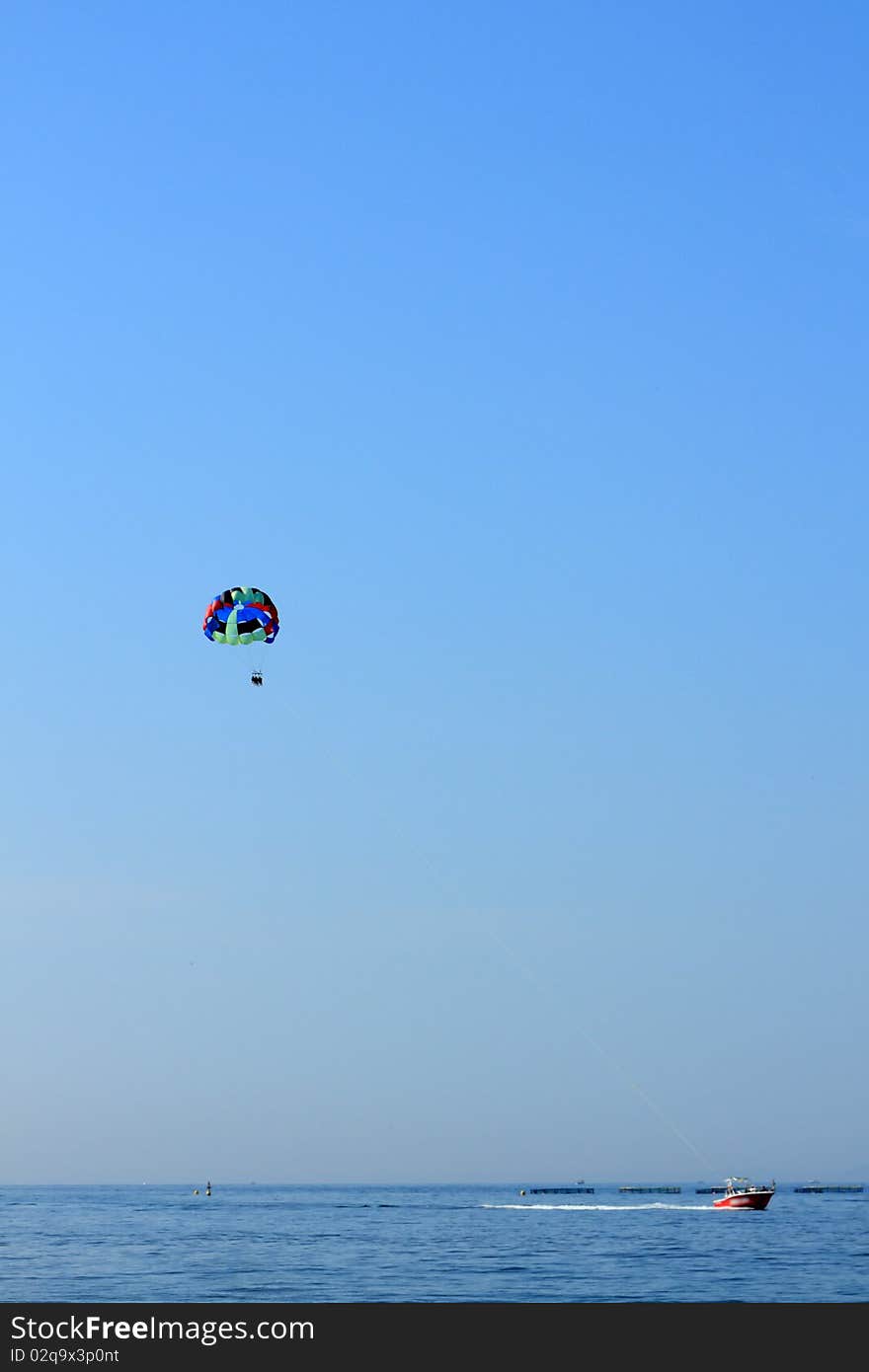 Parasailing over open water with blue sky background and buildings on shoreline in the distance.