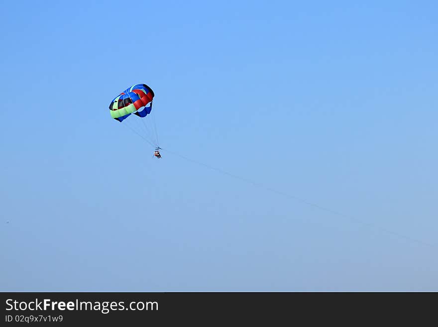 Parasailing over open water with blue sky background and buildings on shoreline in the distance.