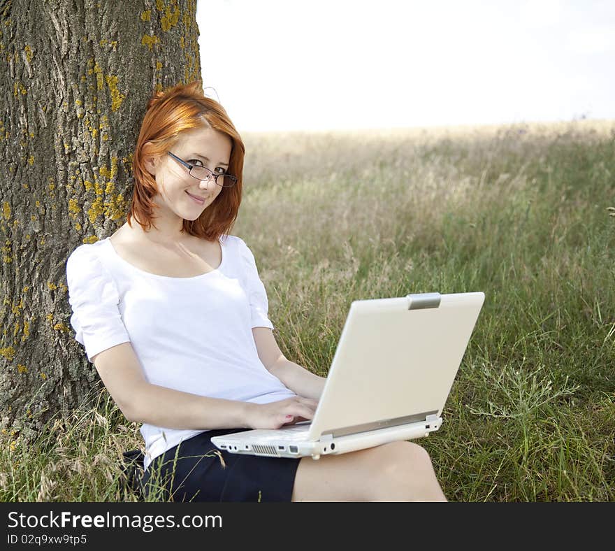 Young Businesswomen in white with glasses and laptop sitting near tree.