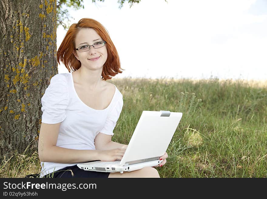 Young Businesswomen in white with glasses and laptop sitting near tree.