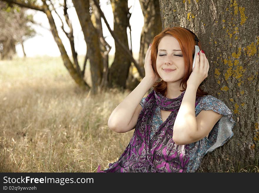 Young smiling girl with headphones near tree. Outdoor photo.