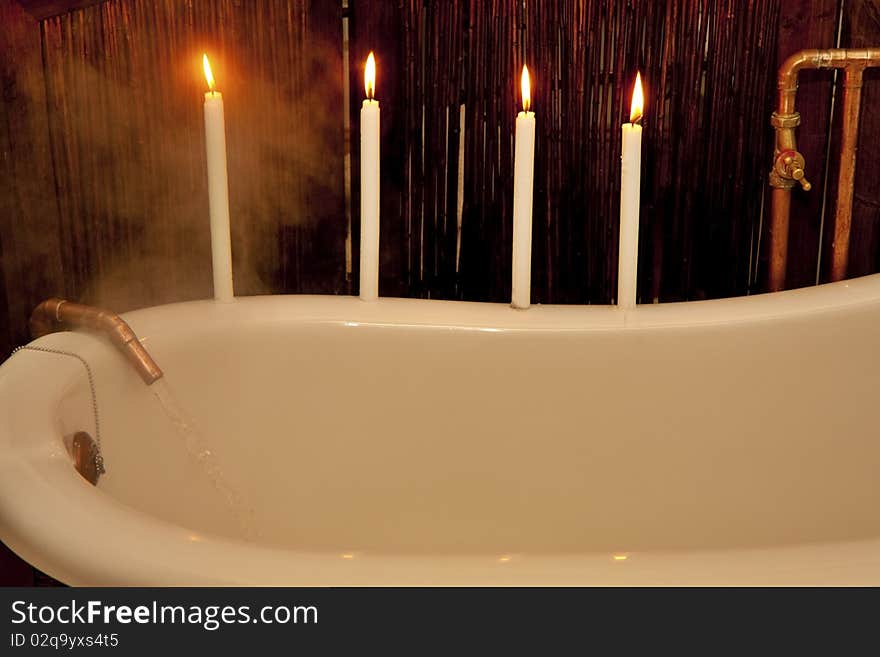 Water pouring into vintage bath from bronze tap with four candles preparing for romantic bath. Water pouring into vintage bath from bronze tap with four candles preparing for romantic bath