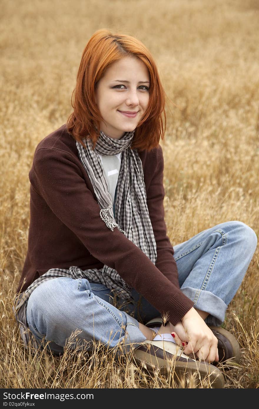 Beautiful red-haired girl at yellow autumn grass. Outdoor photo.