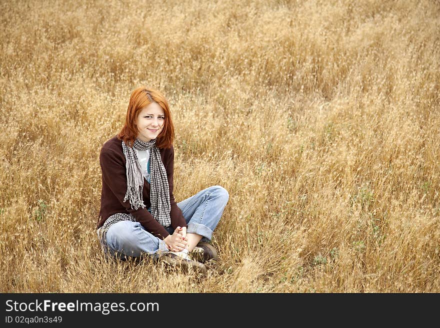 Beautiful red-haired girl at yellow autumn grass. Outdoor photo.