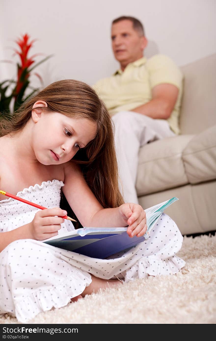 An attractive cute girl doing her homework with her father in the background. An attractive cute girl doing her homework with her father in the background