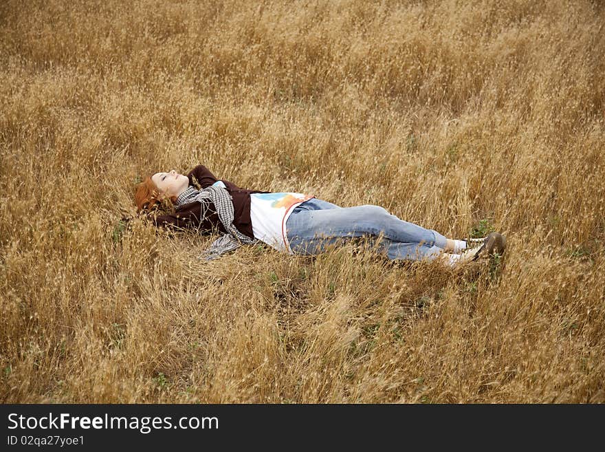 Young beautiful girl lying at yellow autumn field. Outdoor photo.