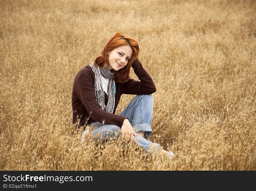 Beautiful red-haired girl at yellow autumn grass.