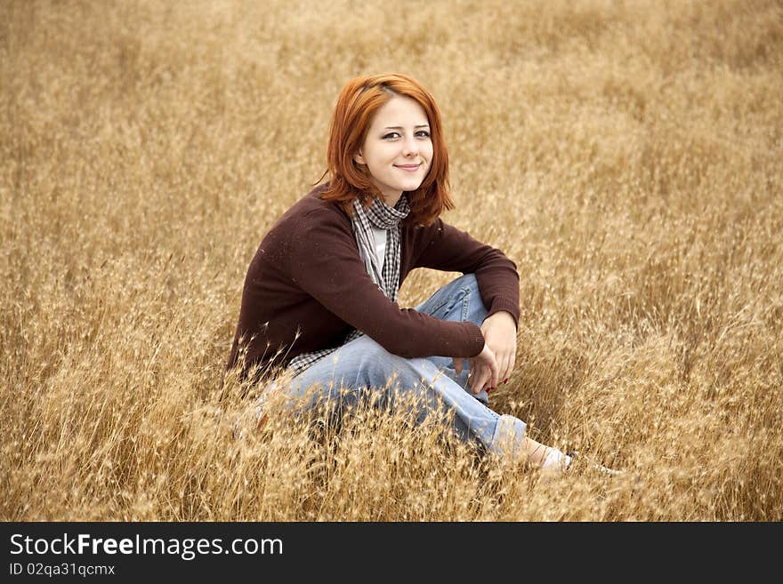 Beautiful red-haired girl at yellow autumn grass. Outdoor photo.