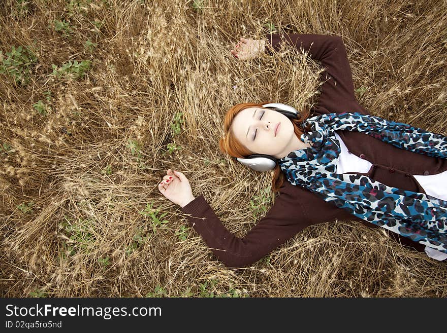 Young girl with headphones lying at field.