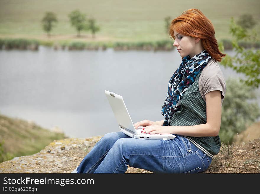 Young beautiful girl with laptop at rock near lake and tree. Young beautiful girl with laptop at rock near lake and tree.