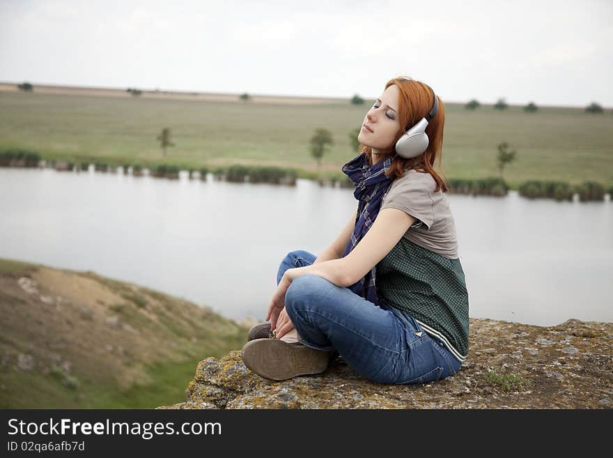 Young fashion girl with headphones at rock near lake. Young fashion girl with headphones at rock near lake.