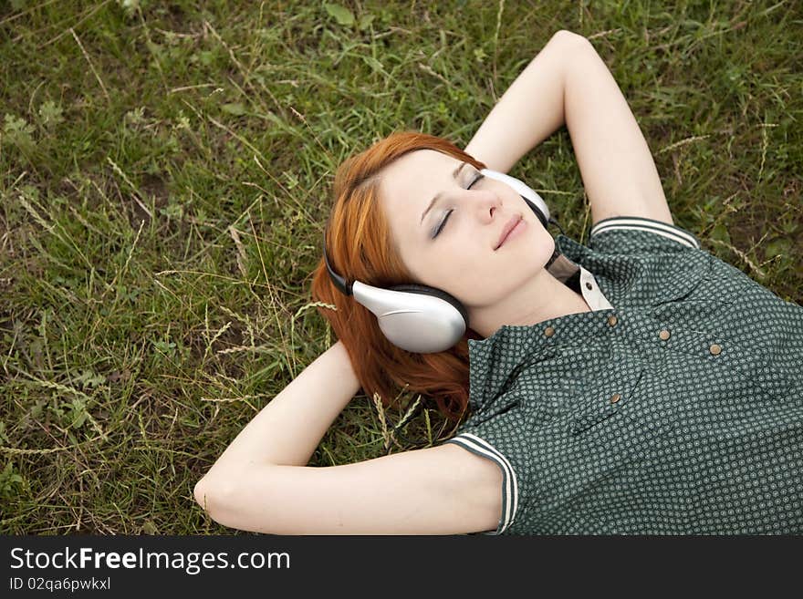 Young fashion girl with headphones lying at green grass.