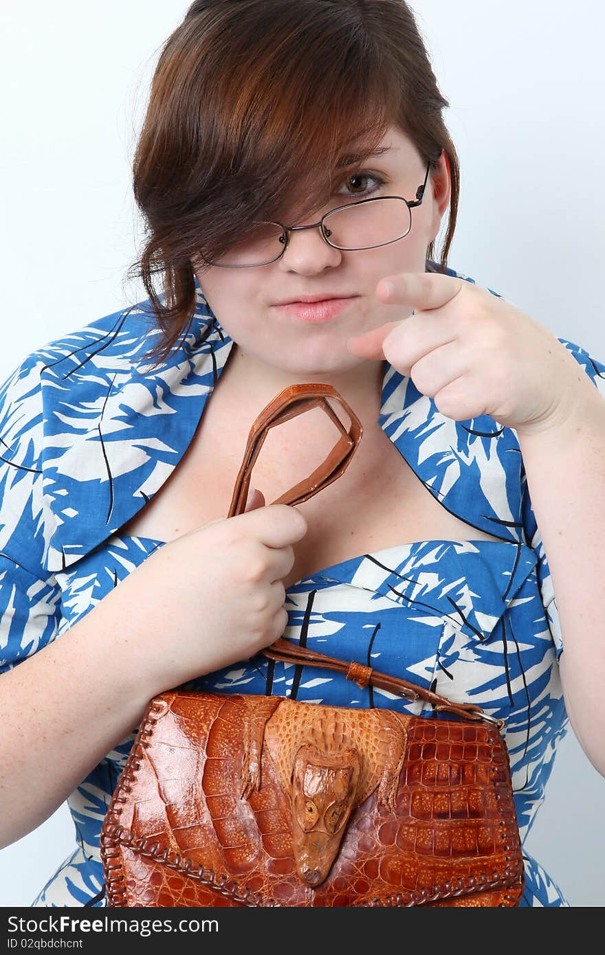 Young woman dressed in retro dress with alligator purse and glasses pointing at camera. Young woman dressed in retro dress with alligator purse and glasses pointing at camera.