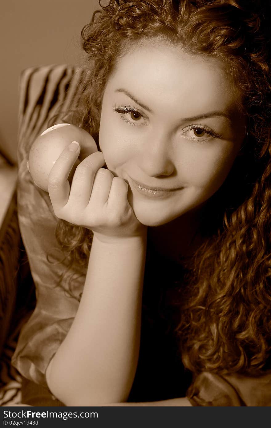 Thinking beautiful young caucasian girl holding apple and smiling sitting in striped old chair. Thinking beautiful young caucasian girl holding apple and smiling sitting in striped old chair