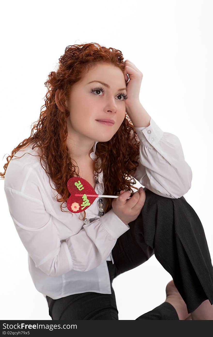 Caucasian pretty red haired girl with colorful bon-bon sitting with smiling facial expression and dreaming isolated on white background. Caucasian pretty red haired girl with colorful bon-bon sitting with smiling facial expression and dreaming isolated on white background