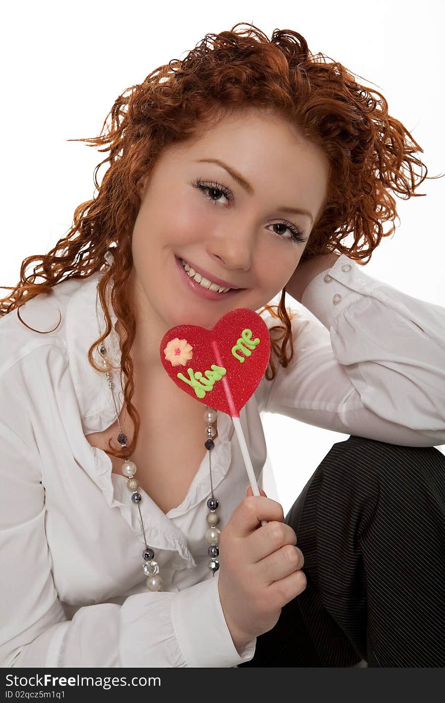 Happy positive looking young caucasian girl with red hair desheveled having fun time with colorful bon-bon sitting isolated over white background. Happy positive looking young caucasian girl with red hair desheveled having fun time with colorful bon-bon sitting isolated over white background