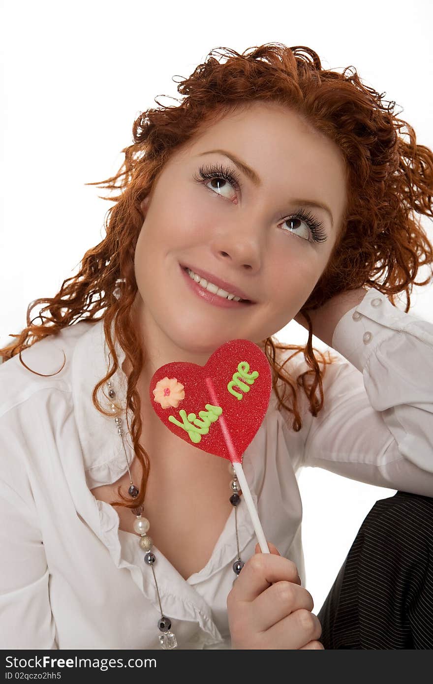 Happy positive looking young caucasian girl with red hair desheveled having fun time with colorful bon-bon sitting isolated over white background. Happy positive looking young caucasian girl with red hair desheveled having fun time with colorful bon-bon sitting isolated over white background