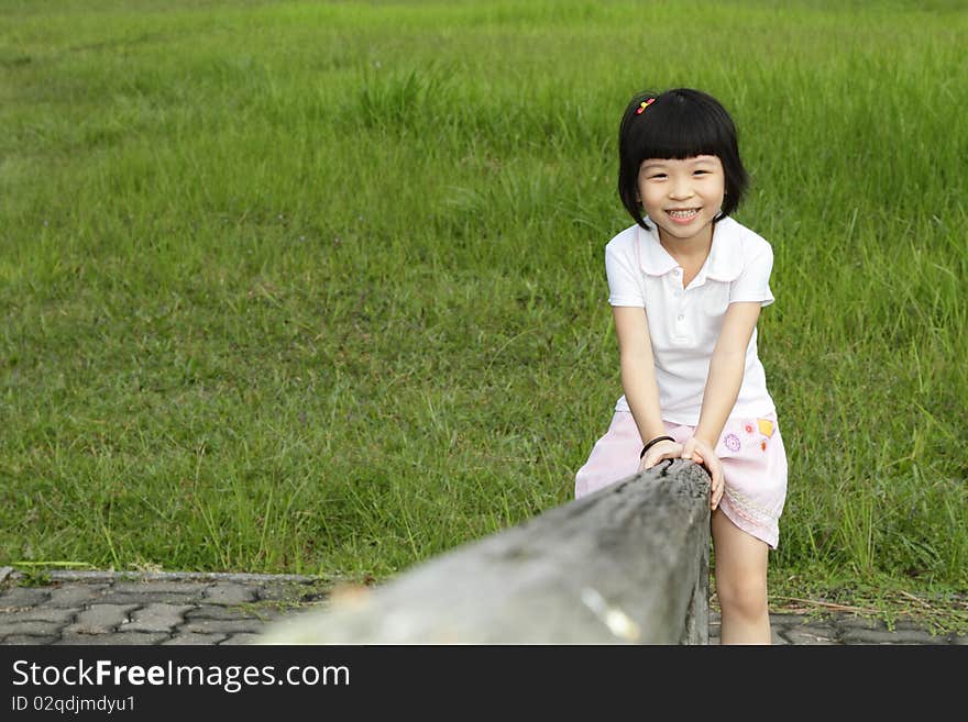 An Asian girl sitting on a wooden beam at a park