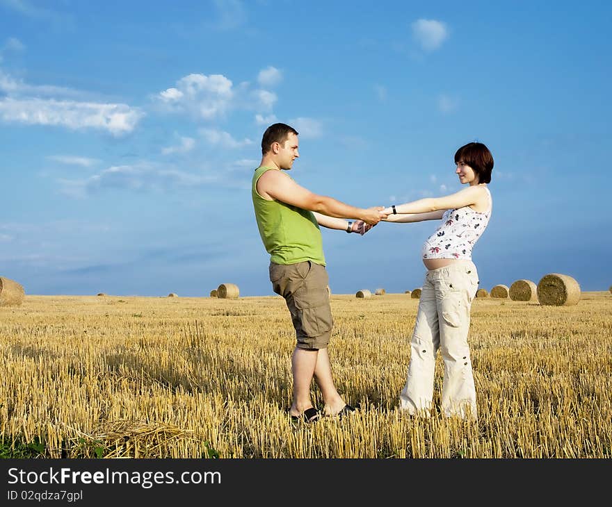 Young couple is staying in the meadow and hold on their hands. Woman is pregnant. Young couple is staying in the meadow and hold on their hands. Woman is pregnant.