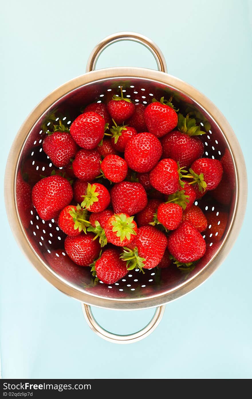 Ripe strawberries in a colander with a blue background