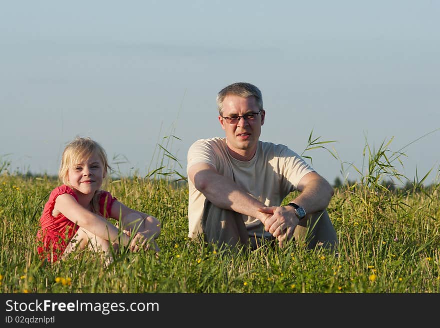 Father with daughter sit on meadow in summer