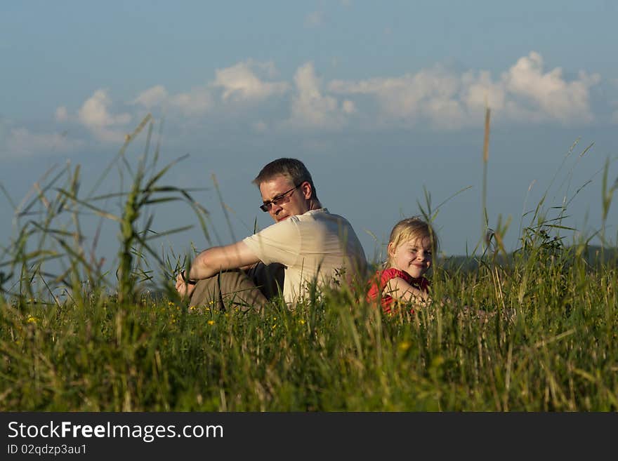 Father with daughter sit on meadow in summer