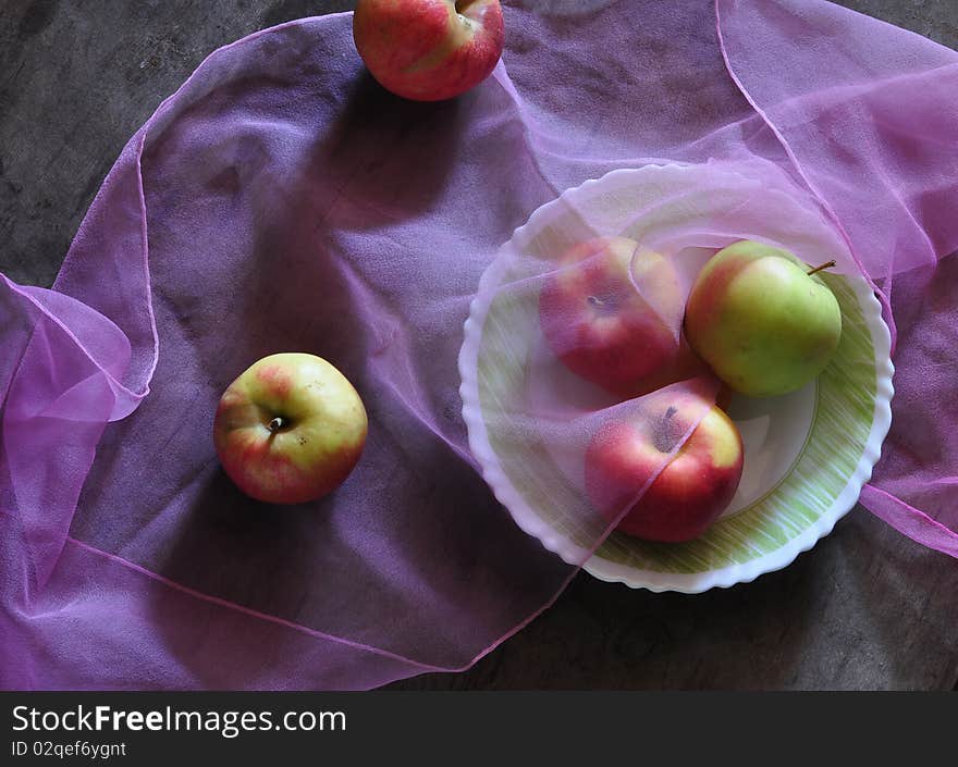 three apples lie on a dish, two apples lie alongside, fabric lies on apples. three apples lie on a dish, two apples lie alongside, fabric lies on apples