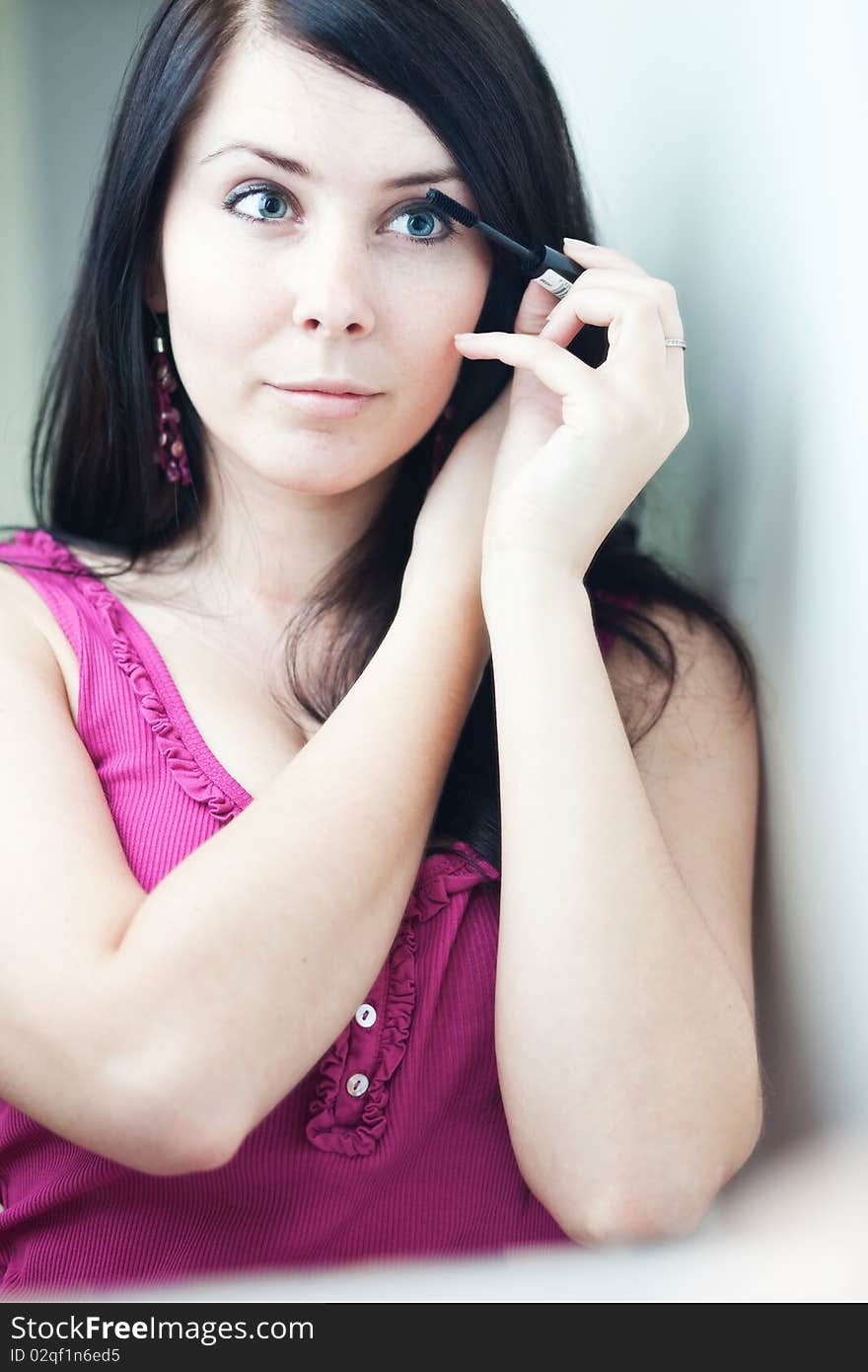 Pretty young woman applying mascara /eye shadows in front of a mirror