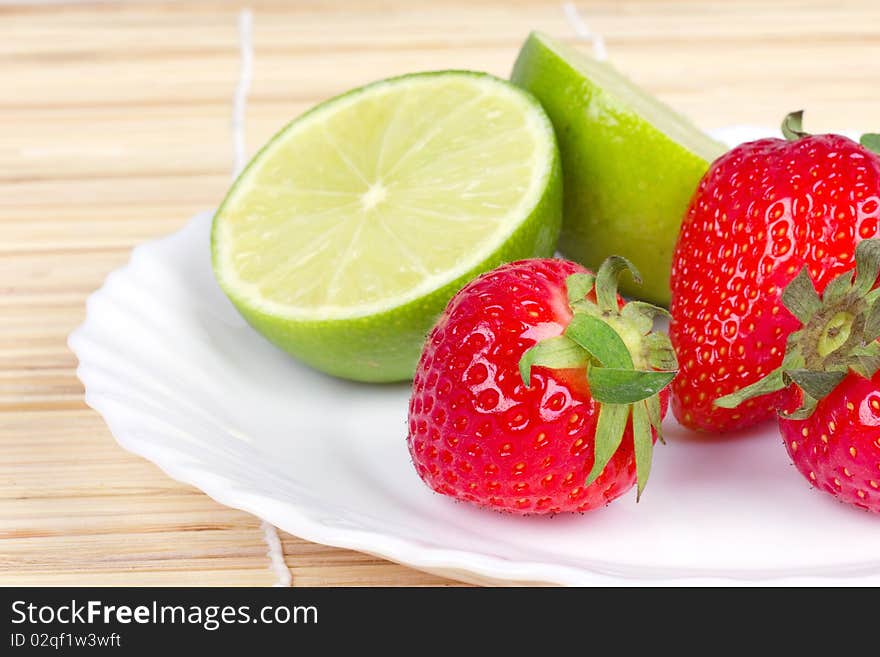 Strawberries and limes on white plate, closed-up