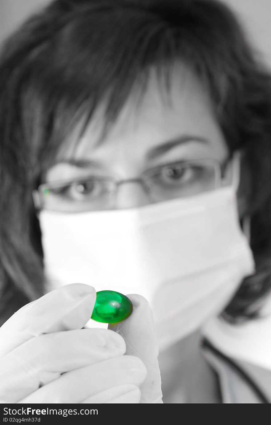 Confident female doctor holding a green pill in black and white