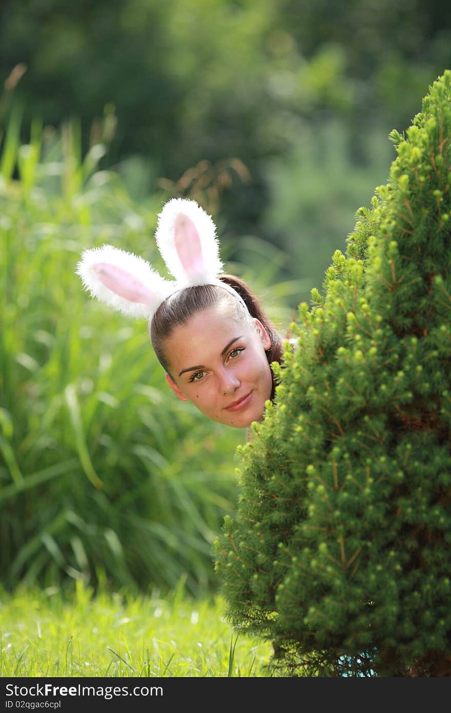 Girl with funny rabbit ears playfully peeking out behind from the tree