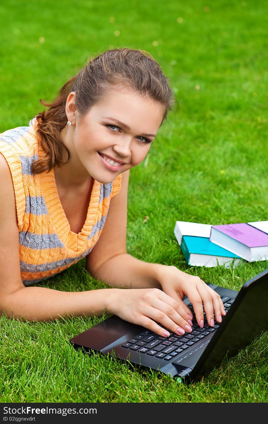 Attractive caucasian girl lying on grass with laptop and smile to the camera. Attractive caucasian girl lying on grass with laptop and smile to the camera