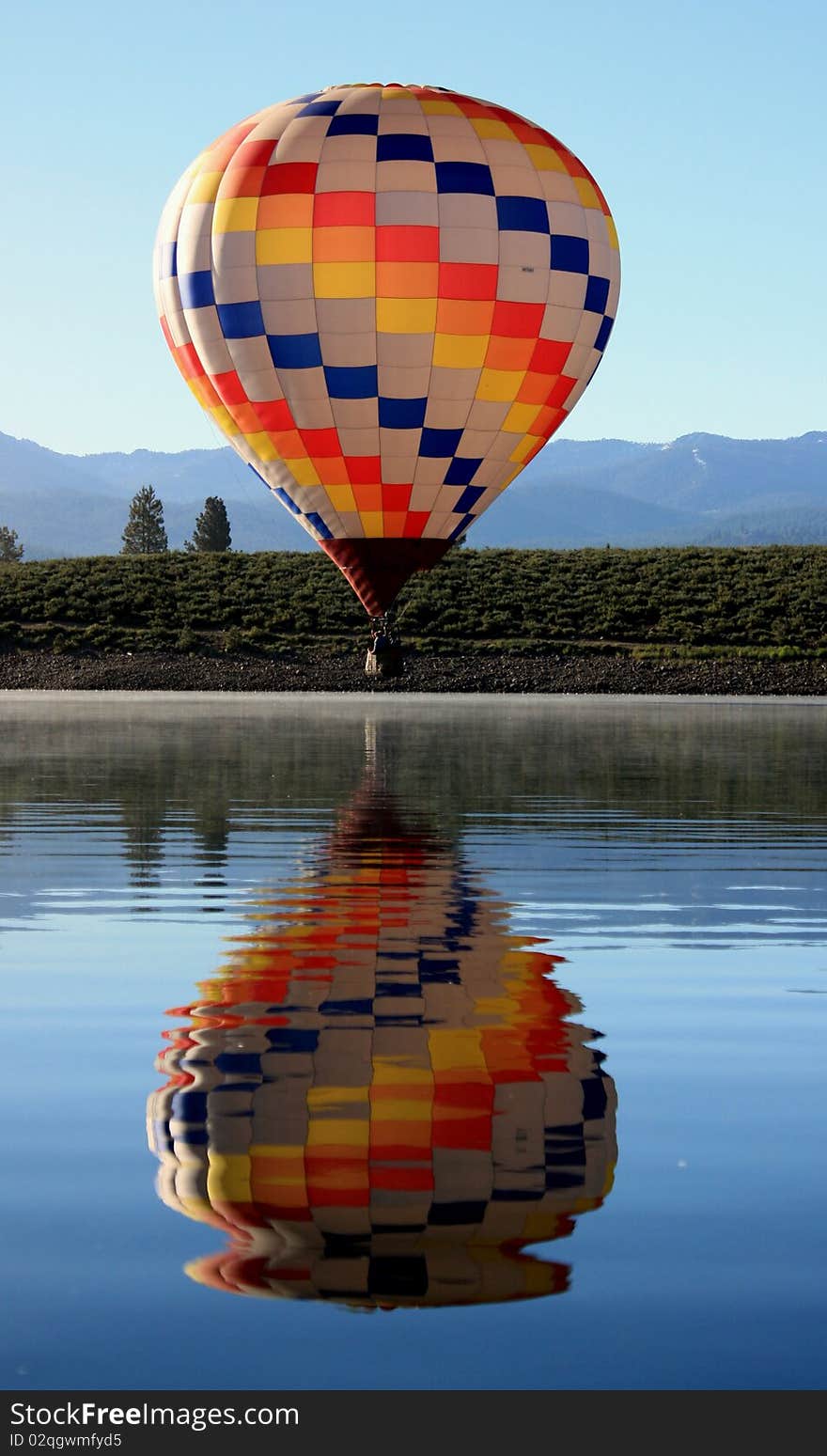 A colorful hot air balloon floats close to the surface of a glassy lake. A colorful hot air balloon floats close to the surface of a glassy lake