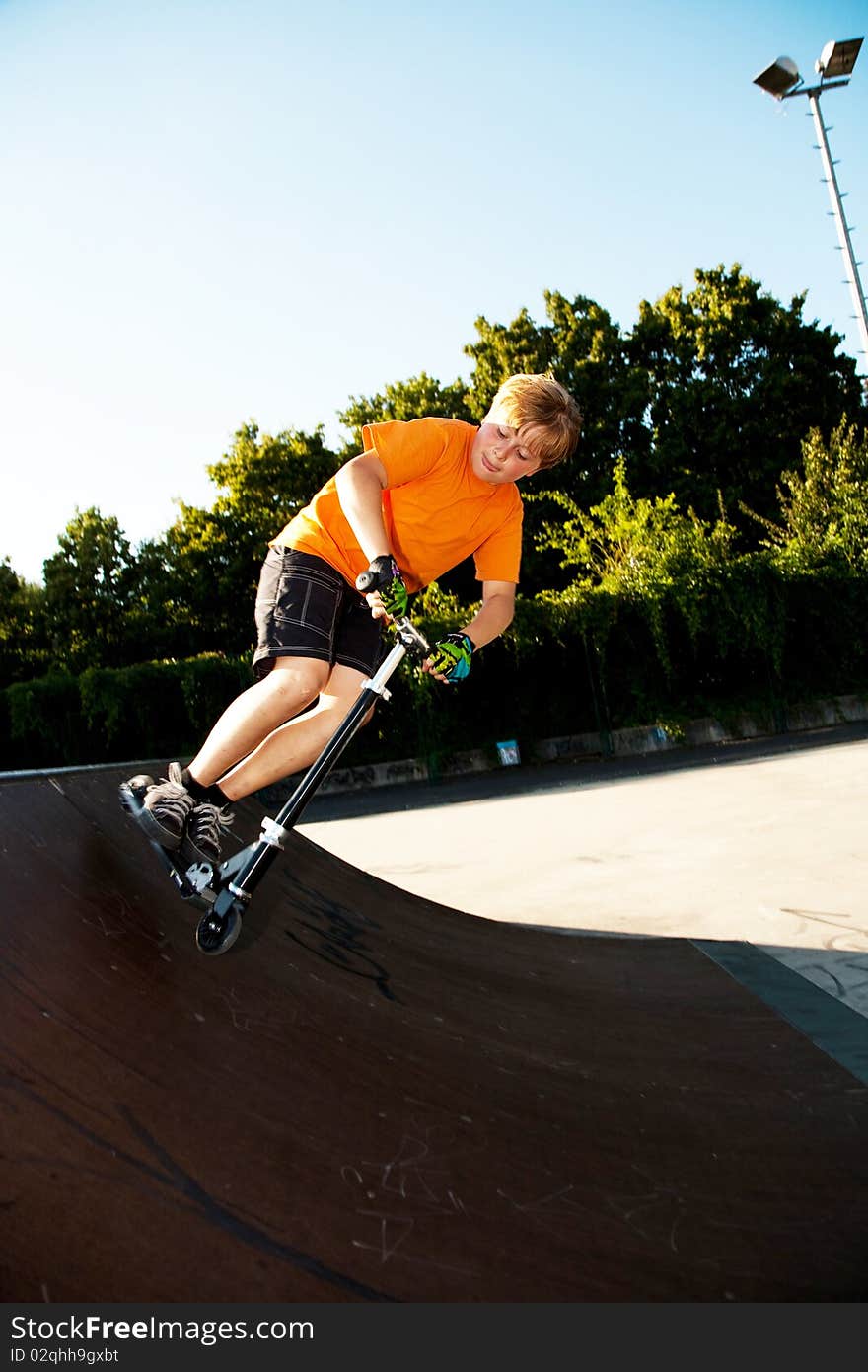 Child with scooter and orange T-shirt is doing tricks at the scateboard parc and enjoying it. Child with scooter and orange T-shirt is doing tricks at the scateboard parc and enjoying it