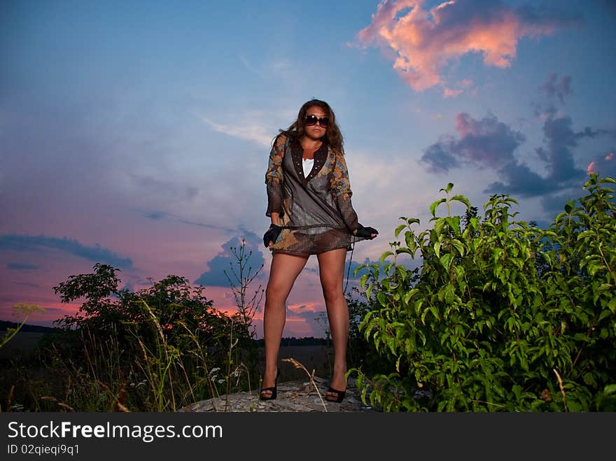 Young woman in sunglasses standing at sunset rock. Young woman in sunglasses standing at sunset rock