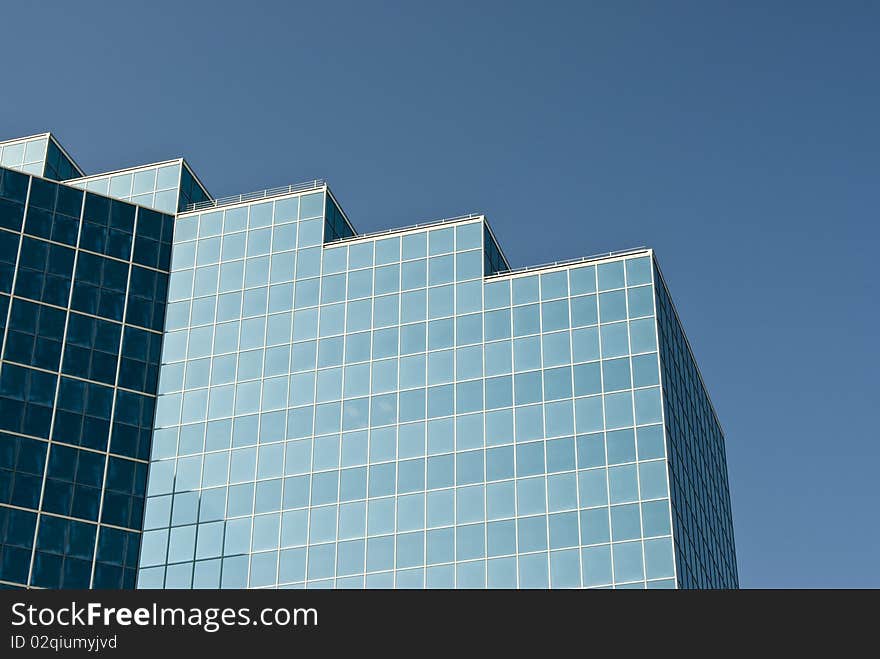 Detail of the architecture of a modern office building with reflective glass exterior windows. Clear blue sky.