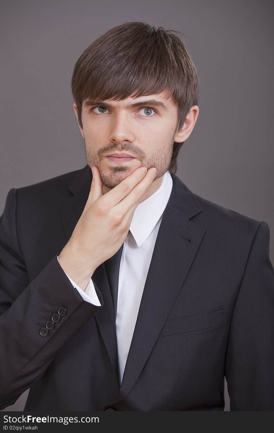 Portrait of young thinking businessman over grey background