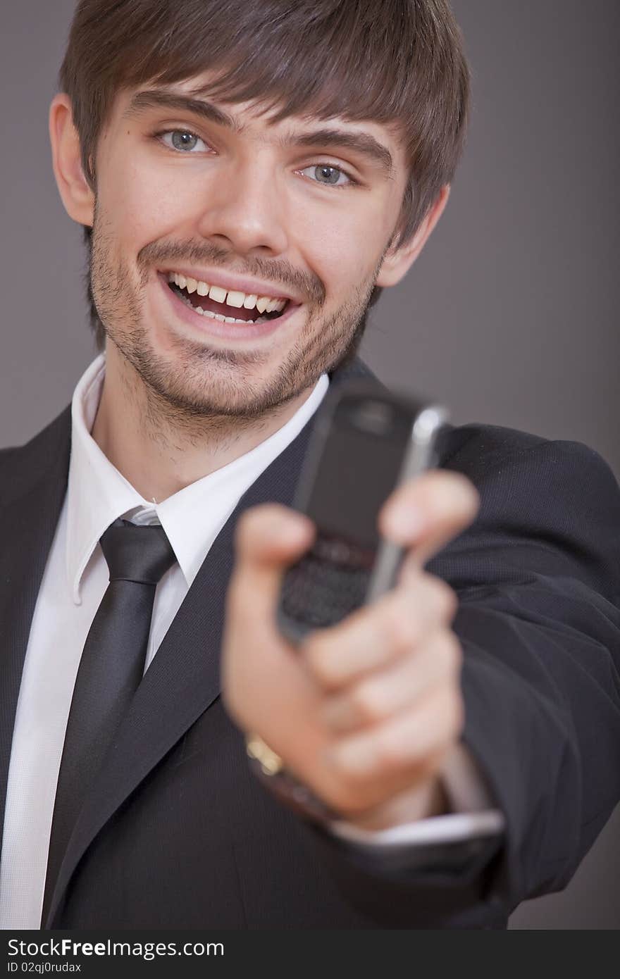 Laughing businessman showing cell phone in the camera over grey background